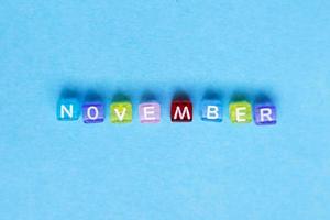 inscripción noviembre hecha con cubos de plástico multicolores sobre un fondo azul.