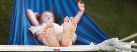 closeup of little girl's feet relaxing in the blue hammock during her summer vacation in back yard photo