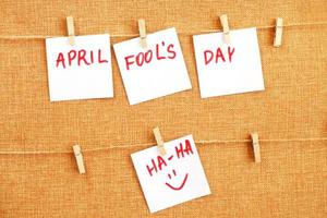 stickers with smiley hanging on the pin and inscription april fools day on brown textile background photo
