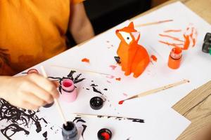 a little boy paints a toy fox made of clay. DIY concept photo