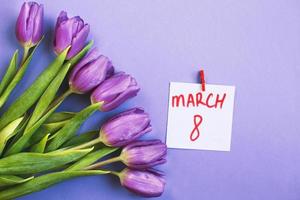 Purple bouquet of flowers tulips background with a note March 8 on veri peri background. photo