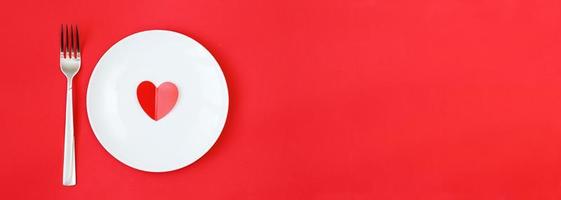 Heart on a white plate with fork on the red background photo