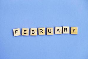 inscription February made by wooden cubes on a veri peri purple background. photo