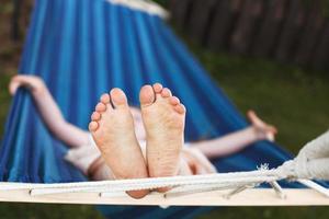 El primer plano de los pies de una niña relajándose en la hamaca azul durante sus vacaciones de verano en el patio trasero foto