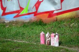 A few used paint cans lie on the ground near the wall with a beautiful graffiti painting. Street art and vandalism concept photo