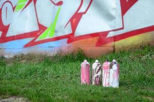 unas pocas latas de pintura usadas yacen en el suelo cerca de la pared con una hermosa pintura de graffiti. concepto de arte callejero y vandalismo foto