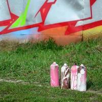 A few used paint cans lie on the ground near the wall with a beautiful graffiti painting. Street art and vandalism concept photo