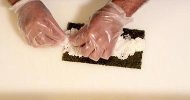chef habilidoso coloca e espalha arroz japonês no nori para rolos de sushi. - tiro de alto ângulo video