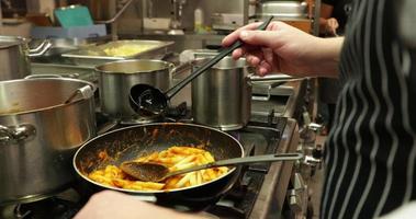 chef ajoutant une louche de bouillon aux pâtes penne dans une casserole - gros plan, ralenti video