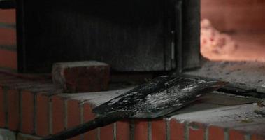 boulanger a mis la pâte à l'intérieur du four à briques à l'aide d'une pelle métallique avec un long manche en bois. - photo en gros plan video