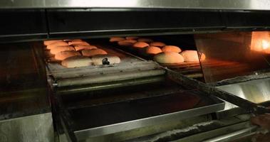 Ein Bäcker zieht manuell den Etagenofenlader und befördert den rohen Brotteig in den Ofen - Brotbacken in einer Bäckerei - Zeitlupe video