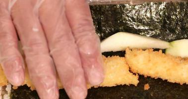 mains avec des gants en plastique jetables roulant des sushis aux crevettes tempura et à l'avocat dans un enveloppement d'algues - photo panoramique à angle élevé video