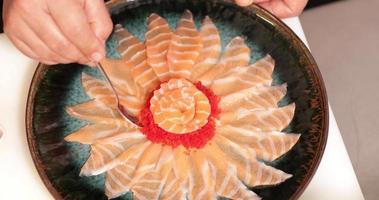 adicionando caviar a um prato de sashimi de salmão fresco em arranjo floral usando uma colher de chá - tiro aéreo video