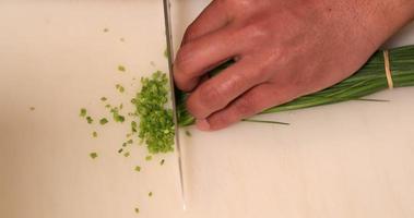 handen van een geschoold chef plakjes de groen ui bieslook snel met een mes Aan een hakken bord in de keuken. - hoog hoek schot video