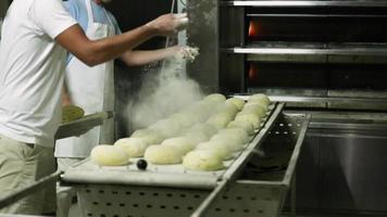 panaderos rociando y salpicando harina sobre la masa en la bandeja para hornear en la panadería. - tiro medio video