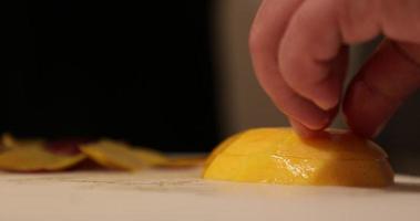 mains coupant la mangue biologique mûre fraîche par un couteau tranchant dans une planche à découper blanche à la cuisine. - photo en gros plan video