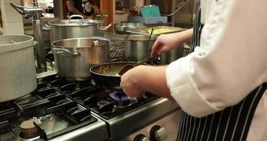 chef cocinando pasta penne en una sartén sobre el fuego en la cocina del restaurante - tiro de zoom lento video