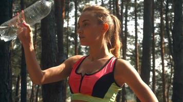 young athletic girl stands in the forest and pours face with water in slow motion video