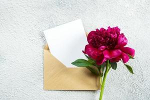 Burgundy peony and empty note card for text on concrete background. Top view, flat lay, copy space photo