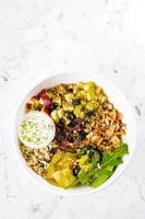 Salad lunch bowl with mix salad, chicken breast, apple, pineapple, raising, dates, brown rice and walnut. Keto salad in bowl on marble background. Top view, copy space. Concept of healthy food photo
