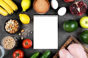 Keto diet food concept. Meat, raw vegetables, nuts and fruits on slate table background. Top view, copy space. Mockup concept with notebook. photo