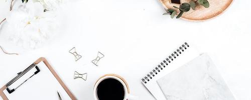 Banner image. Workplace with eucalyptus, peony, clipboard, notebook, cup of coffee, and pen. photo