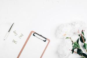 Flat lay Office table desk. Workplace with flowers peonies, clipboard and pen. Mockup photo