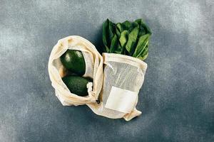 Avocado and spinach in eco cotton bags on table. Zero waste shopping concept. Flat lay, top view photo