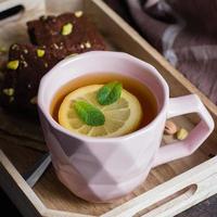 Tea with lemon and mint leaf with homemade biscuit brownie with pistachios for Breakfast on wooden tray on stone table background. Close-up photo