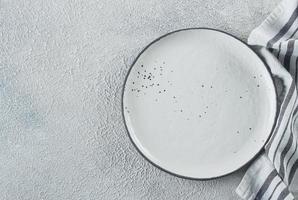 Menu Recipe Concept. Empty ceramic plate, kitchen towel on light concrete background. Copy space. photo
