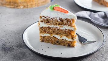 Slice of homemade carrot cake with cream cheese frosting on plate on gray stone table background. photo