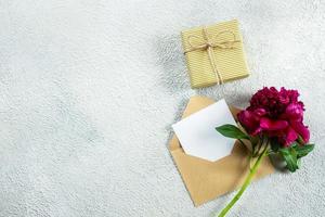 Mothers day or Womens day concept. Burgundy peony and empty note card for text on concrete background. Top view, flat lay, copy space photo