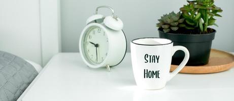 Morning home routine. White cup and alarm clock on bedside table photo