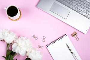 Office table desk. Workplace with laptop, cup of coffee, flowers peonies, pen. Flat lay, mockup photo