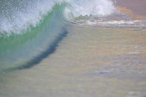 una ola rompiendo en la orilla de arena foto