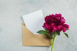 Burgundy peony and empty note card for text on concrete background. Top view, flat lay, copy space photo