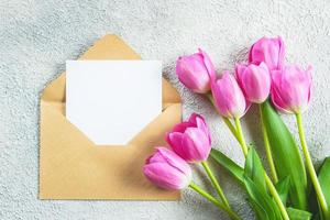 Mother's day Holiday Concept. Pink tulips flowers and empty card on concrete background. Greeting card for Womens or Mothers Day. Flat lay, top view, copy space. Mockup concept. photo