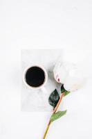 taza de café, cuaderno y flores de peonía blanca sobre fondo de mesa rosa. acogedor, bodegón, mínimo foto