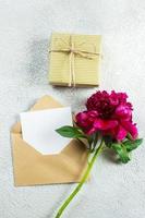 Mothers day or Womens day concept. Burgundy peony and empty note card for text on concrete background. Top view, flat lay, copy space photo