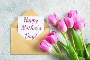 concepto de vacaciones del día de la madre. flores de tulipanes rosas y tarjeta sobre fondo de hormigón. tarjeta de felicitación para el día de la mujer o de la madre. endecha plana, vista superior. foto