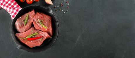 Raw meat. Raw beef steak on a black board with herbs and spices. Top view. Banner for design photo