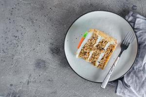 Slice of homemade carrot cake with cream cheese frosting on plate on gray stone table background photo