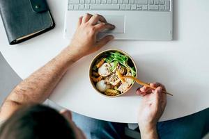 Eating healthy lunch bowl in man' s hands. Home office, food delivery, detox, food concept photo