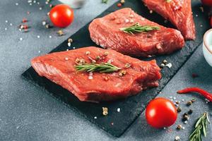 Raw meat. Raw beef steak on a black board with herbs and spices. Close-up photo