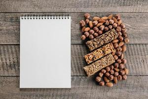 Health Bars, Mixed Nuts and White Empty Notebook Blank For Text. Energy bars with almond and hazelnuts. Snack for healthy still life. Top view, copy space photo
