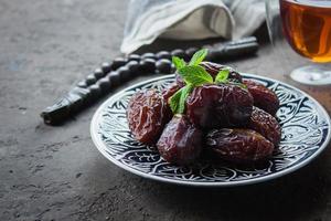 Ramadan kareem food concept. Fresh Dates, rosary beads and tea on dark concrete background photo