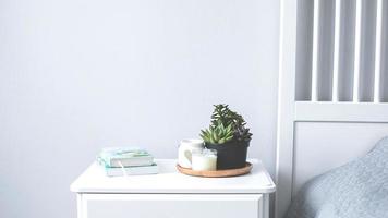 Tiny succulents, candles and books on bedside table in the bedroom in scandinavian style home. Scandinavian interior in gray and white colors photo