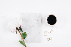 taza de café, cuaderno y flores de peonía blanca sobre fondo de mesa rosa. acogedor, bodegón, mínimo foto