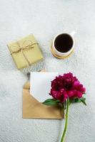 Flat lay with burgundy peony, cup of coffee and empty note card for text on concrete background. Top view, flat lay, copy space. Mothers day or Womens day concept. photo