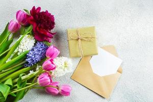 Mother's day or Woman's Day Concept. Hyacinth, tulips and pion flowers, empty card and gift present on ligth concrete background. Spring Greeting card. Flat lay, top view, copy space. Mockup concept. photo